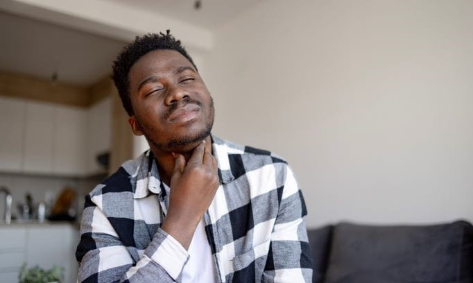 Black man in living room with hand raised to throat due to heartburn symptoms