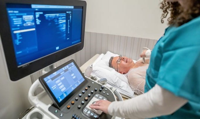 female in scrubs giving echocardiogram to a man on his back in a hospital bed