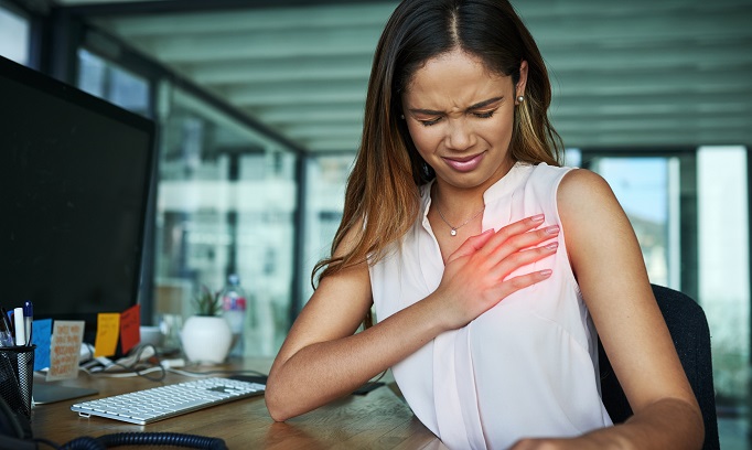 Woman at her desk pressing against her chest in an attempt to relieve her heartburn