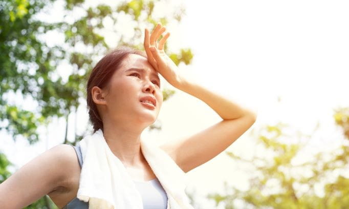 woman with towel around neck and hand to forehead suffering from heat related illness