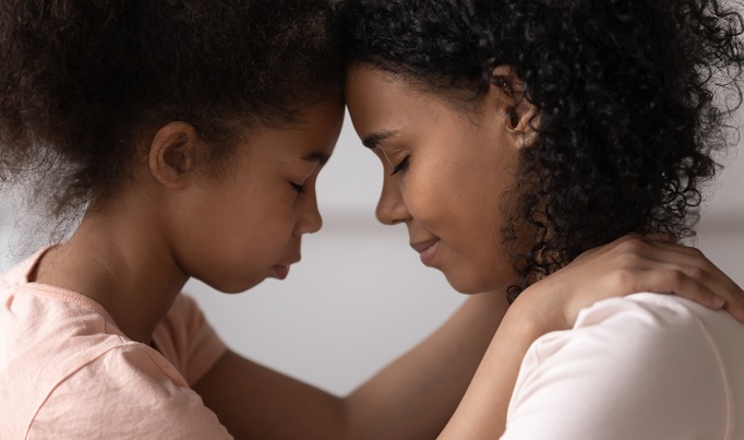 an african american mother and daughter touch foreheads while talking