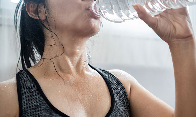 Sweaty woman who is exercising outdoors in summer guzzles water to avoid dehydration