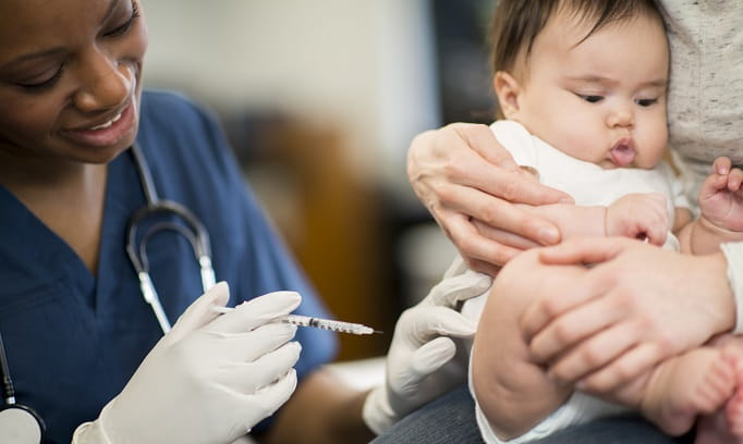 young child getting vaccinated by african american nurse