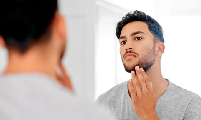 young man looking at reflection with hand touching his beard