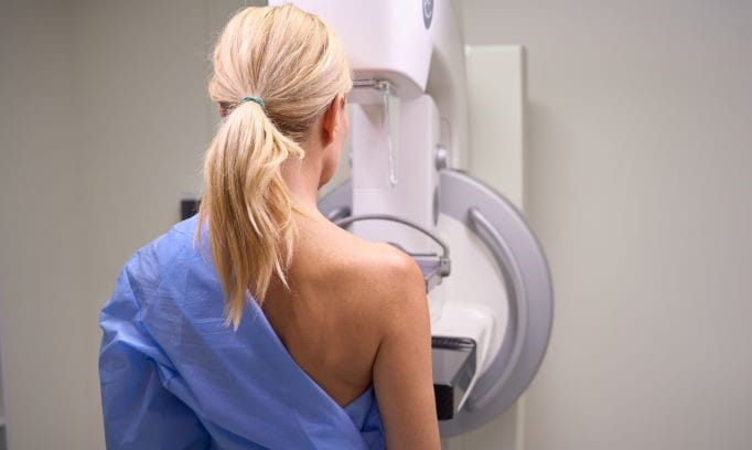 back view of a robed female patient getting 3d mammogram in radiology room