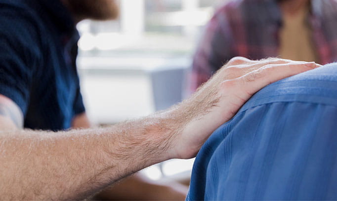 A person placing their hand on someone else's shoulder in who is speaking about mental health stigma