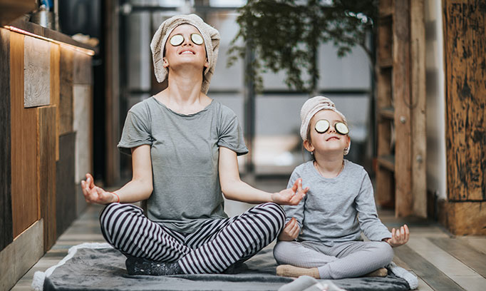 mom and daughter in yoga pose with cucumber slices over their eyes