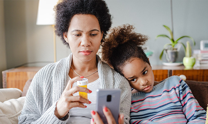 mother with sick child looking at prescription bottle and using smartphone