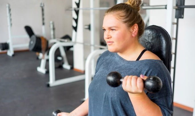 seated woman doing bicep curls in gym setting 
