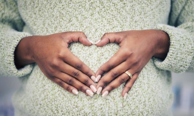 pregnant person making heart shape with hands on her belly