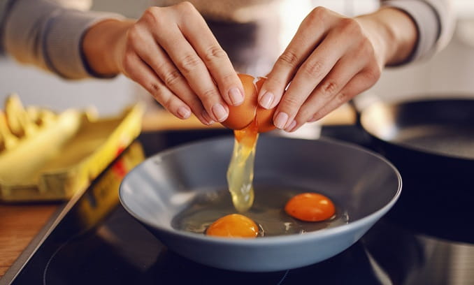 woman fries two eggs in a light blue fry pan as she tries to eat more protein 682x408
