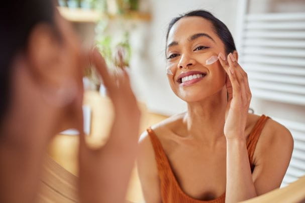 a young woman looking in the mirror applying sunscreen to her face