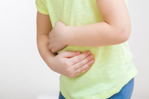 A small child in a green shirt and blue pants holding their stomach in pain.