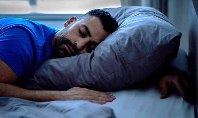 man sleeping in bed comfortably on side with head resting on pillow