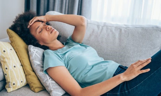 young woman lying on couch holding her head with hand