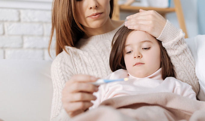 Mom checking her daughters temperature with a thermometer wondering if its the flu or a cold 