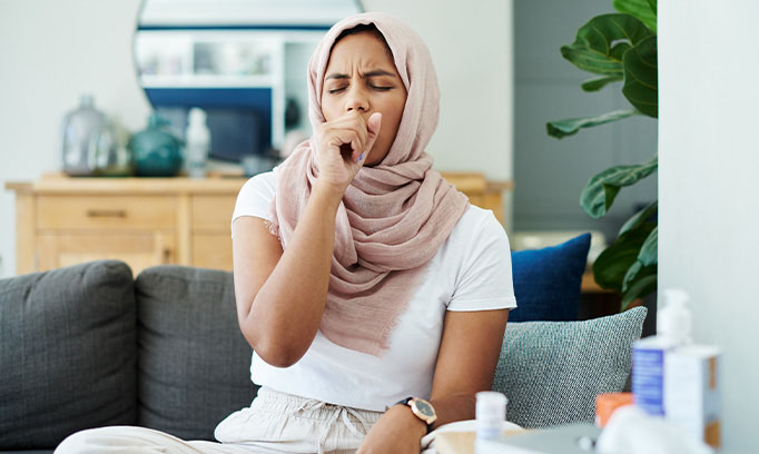 young woman in head scarf coughs and wonders if she should see a doctor
