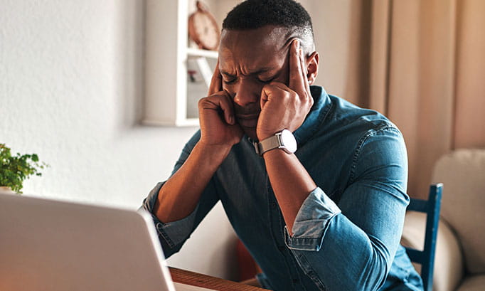 Man working at his desk pressing his fingers against his temples due to migraine symptoms