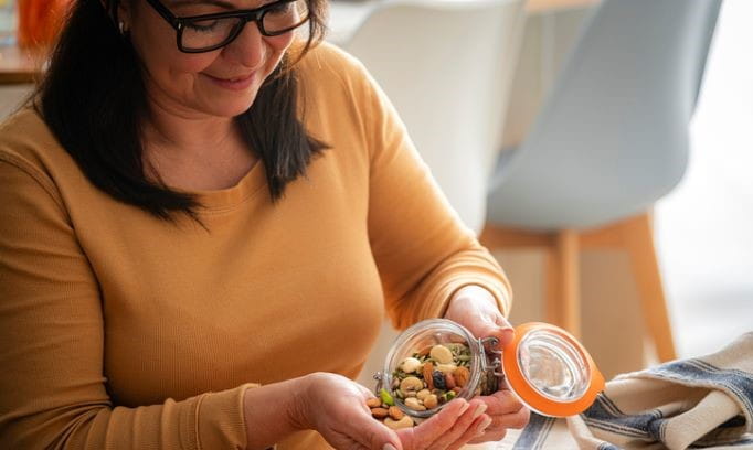 A woman pouring a container of mixed nuts and seeds into her hand to eat as a snack.