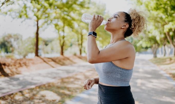 Female jogger takes a sip of water after running in the park.