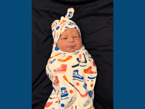 Baby boy swaddled in a blanket with ice hockey images on it.