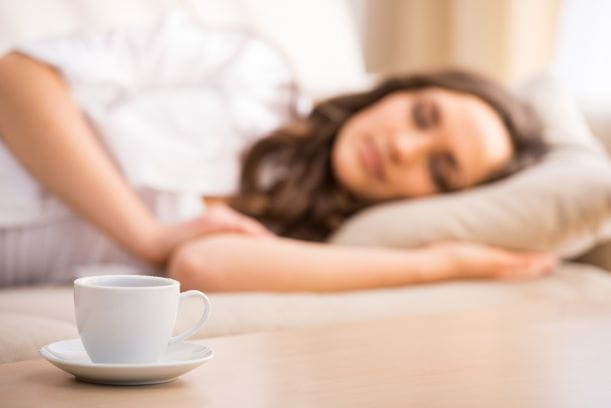 coffee cup on a small table with a young woman sleeping on a couch nearby 