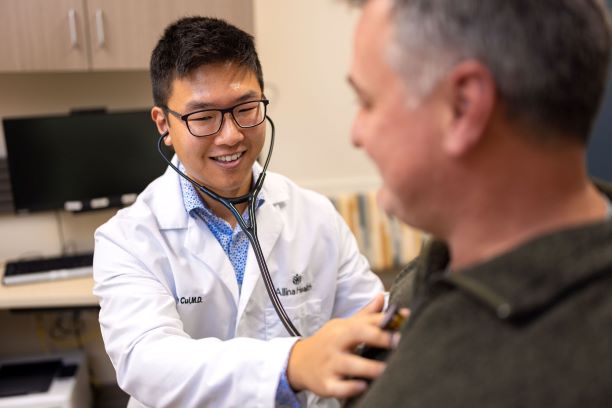 male doctor listens to adult male patient’s heart using a stethoscope 