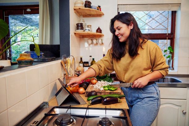 young woman using her digital tablet while preparing a healthy meal at home