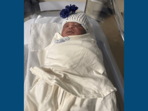 Newborn baby swaddled in a white blanket in a hospital basinet. 