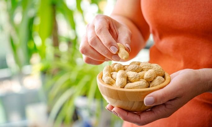 Woman holding a bowl full of unshelled peanuts.