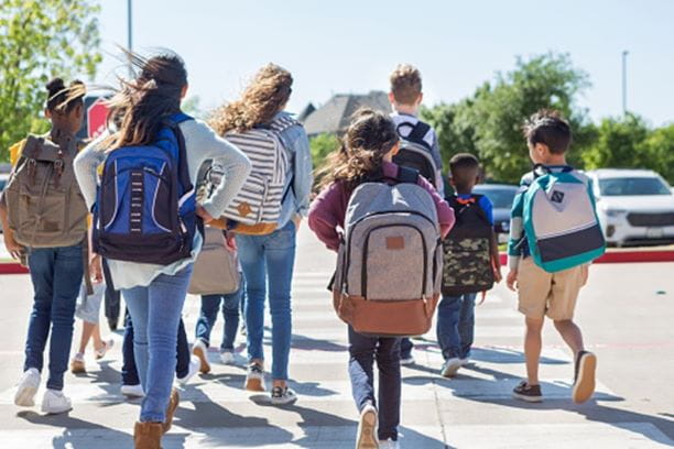 Nine children, of all ages, walking across a crosswalk to school.