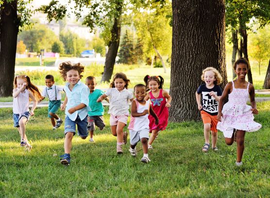 Multiple children of various races running around together in the summer on a grassy field