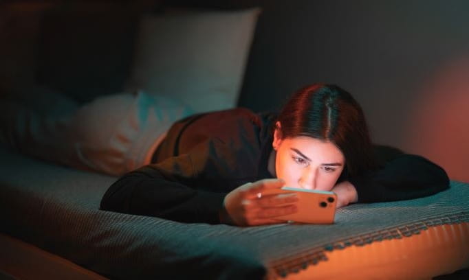 Teen lies in bed on phone because of social media addiction.