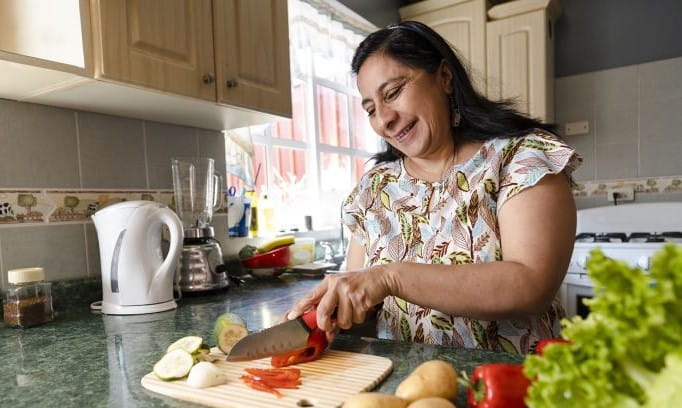 woman at kitchen counter chopping a red pepper using food as medicine